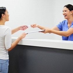 Smiling dental assistant handing patient form