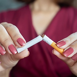 a person breaking a cigarette to maintain healthy dental implants