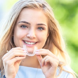 woman smiling while holding Invisalign aligner