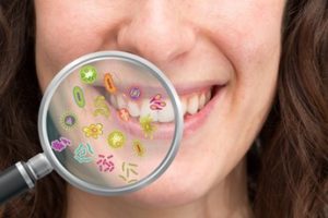 A magnifying glass with cartoon bacteria is being held up to a woman’s smile