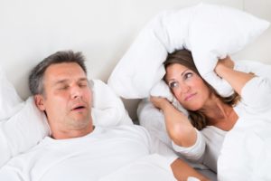 Man snoring and woman covering head with pillow