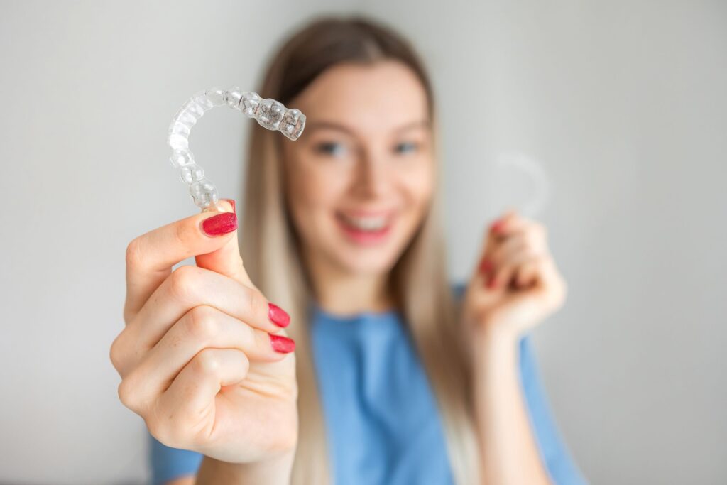 Woman in blue shirt with red nails holding clear aligners
