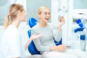 Blond dentist showing blond patient her results with handheld mirror